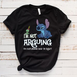 May include: Black t-shirt featuring a blue cartoon character and a green alien. The text "I'M NOT ARGUING I'M EXPLAINING WHY I'M RIGHT" is printed in white. The shirt is made of a soft material.
