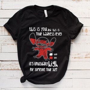 May include: Black t-shirt with a red cartoon character and the text "this is you and this is your badness level. It's unusually high for someone your size." The character has a red body and white eyes. There is a scale below the character with the words "good" and "bad" next to it.