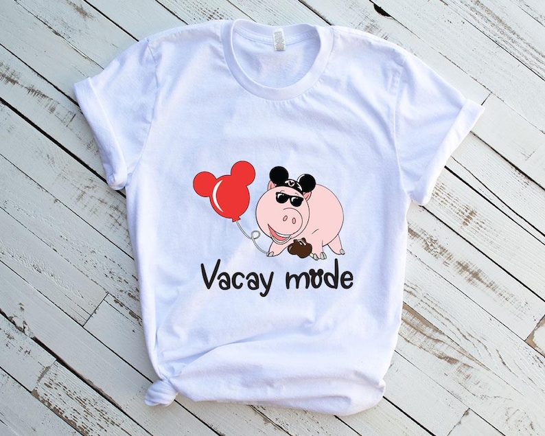 May include: White t-shirt with a cartoon pig wearing sunglasses and a Mickey Mouse hat. The pig is holding a red balloon with Mickey Mouse ears. The text "Vacay mode" is printed below the pig.
