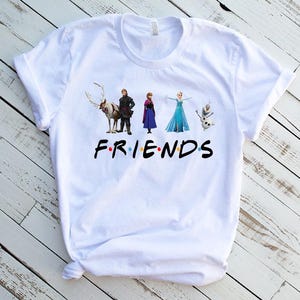 May include: White t-shirt with a graphic of characters from the movie Frozen. The characters are standing in a line and the text "FRIENDS" is below them.