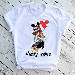 Puede incluir: Camiseta blanca con una imagen de dibujos animados de un personaje con un sombrero de Mickey Mouse y sosteniendo un globo rojo. El texto "Vacay mode" est&aacute; impreso debajo de la imagen.