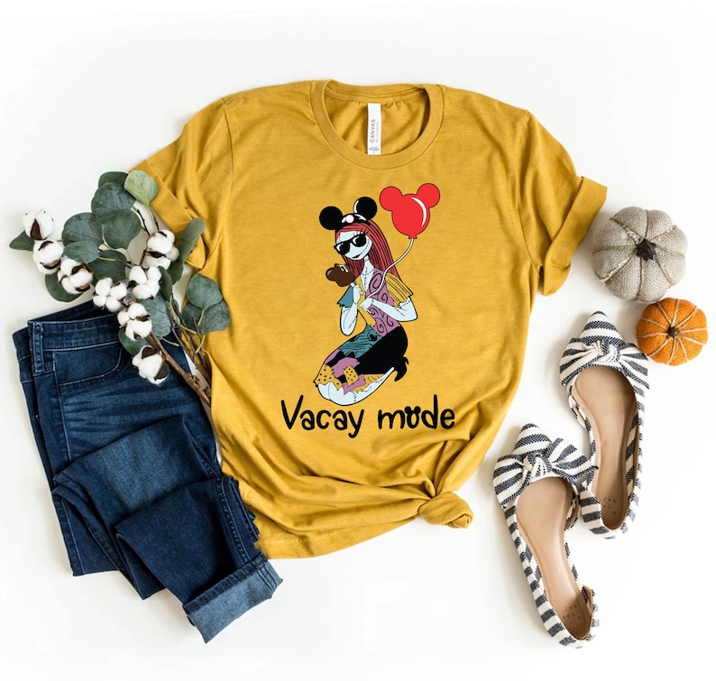 Puede incluir: Una camiseta amarilla mostaza con un gr&aacute;fico de un personaje de dibujos animados con gafas de sol y un sombrero de Mickey Mouse sosteniendo un globo rojo. El texto "Vacay mode" est&aacute; impreso debajo del gr&aacute;fico.