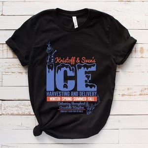 May include: Black t-shirt with a blue and white graphic of Kristoff and Sven's Ice Harvesting and Delivery. The text says "Delivering throughout Arendelle Kingdom. Contact Sven for details."