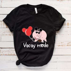 May include: Black t-shirt with a cartoon pig wearing sunglasses and a Mickey Mouse hat. The pig is holding a red balloon and the text "Vacay Mode" is printed below the pig.