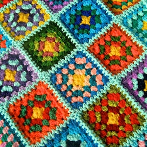 Könnte beinhalten: Eine bunte gehäkelte Decke mit verschiedenen Quadraten in unterschiedlichen Farben, darunter Rot, Grün, Blau, Gelb und Lila.