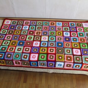 Puede incluir: Una manta de ganchillo colorida hecha de cuadrados en varios tonos de rojo, verde, azul, rosa y blanco.