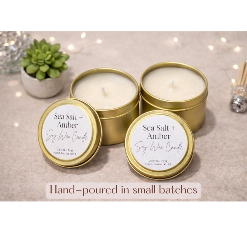May include: Four gold-colored, round soy wax candles with white wax and wicks. The labels read "Sea Salt + Amber Soy Wax Candle" and "Hand-poured in small batches". Each candle is 2.50 oz / 70 g.