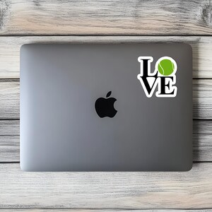 May include: A silver laptop computer with a black Apple logo and a sticker that says "LOVE" with a green tennis ball in the "O".