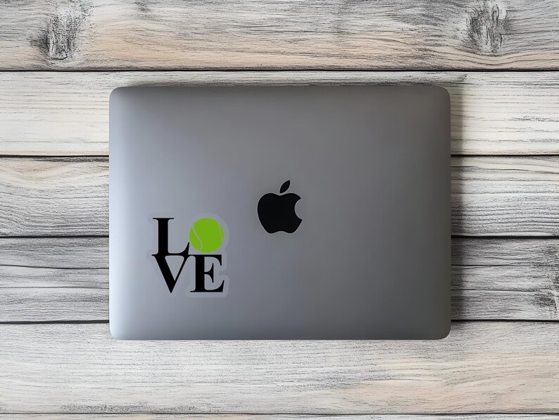 May include: A laptop computer with a black and white sticker that says "LOVE" with a tennis ball in the "O". The sticker is on the silver laptop.