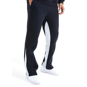 May include: Black sweatpants with a white and gray stripe down the side. The pants have a relaxed fit and are paired with white sneakers. The design features a contrasting color panel that runs along the outer seam of each leg.