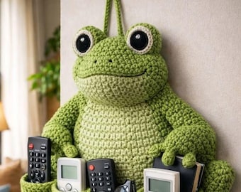 May include: A whimsical, handmade crochet frog wall organizer in shades of green. The frog has large, expressive eyes and holds four pockets, perfect for storing remotes, glasses, and small items. A fun and functional home decor piece.