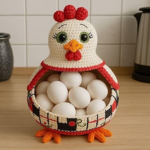 May include: A handcrafted crochet chicken-shaped egg basket. The basket is cream-colored with red and black accents, holding several white eggs. The chicken has a red comb, orange beak, and green eyes. The basket is sitting on a wooden surface.