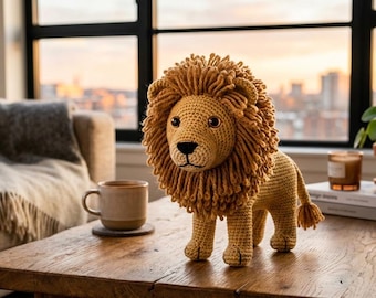 May include: A crocheted lion with a golden mane and body stands on a wooden table. The handmade lion has a detailed face with dark eyes and a small tail. The lion is a decorative item, perfect for a nursery or children's room.