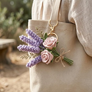 Peut inclure: Un sac fourre-tout beige avec un porte-clés doré tenant un bouquet de lavande et de roses roses. Le bouquet est noué avec de la ficelle et des tiges vertes. L'arrière-plan est une scène extérieure floue.