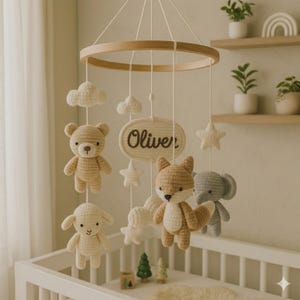 Op de afbeelding: Een handgemaakte baby mobile met gehaakte dieren, wolken en sterren die aan een houten ring hangen. De mobile bevat een beer, een vos, een olifant en een lam, met de naam "Oliver".