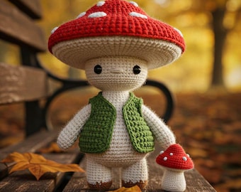 May include: A crocheted mushroom figure with a red cap and white spots, wearing a green vest. A smaller mushroom figure is next to it. The figures are on a wooden bench with autumn leaves.