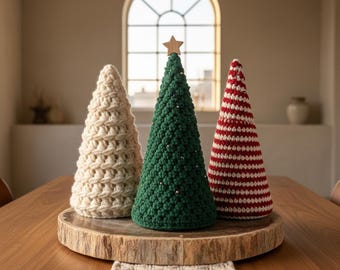 May include: Three handmade crochet Christmas trees in cream, green, and red and white stripes. The green tree has a wooden star on top and silver beads. The trees are displayed on a wooden slab, perfect for holiday decor.