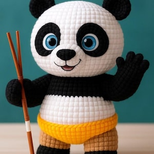 May include: A handmade crochet panda bear with black and white fur, blue eyes, and a yellow waistband. The panda is holding two brown chopsticks and waving. The panda's design is a cute and cuddly toy.