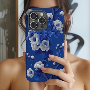 May include: A blue phone case featuring a floral design with white and blue flowers. The case has a glossy finish and covers the back and sides of the phone. The floral pattern is detailed and covers the entire surface of the case.