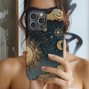 Pode incluir: Uma capa de smartphone com um design celestial. Apresenta um sol dourado, lua, estrelas e nuvens contra um fundo azul-petróleo escuro. A capa tem uma estética vintage detalhada, com linhas intrincadas e uma aparência texturizada.