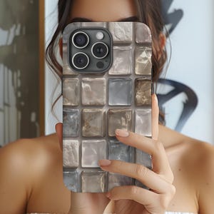 Könnte beinhalten: Eine Smartphone-Hülle mit einem Mosaikfliesen-Design in Grau-, Beige- und Weißtönen. Die Hülle hat ein quadratisches Muster und einen Kameraausschnitt. Die Handyhülle wird vor einer Person hochgehalten.