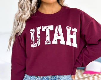 May include: Burgundy sweatshirt with a white distressed graphic that says "UTAH" in a collegiate font.