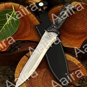 May include: A hunting knife with a silver blade and a black wooden handle, resting in a black leather sheath. The knife has a serrated edge and a decorative emblem. The background is a wooden surface.