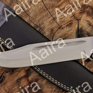 May include: A large, stainless steel knife with a black handle and a leather sheath. The blade is wide and curved, with a polished finish. The sheath is black with white stitching.