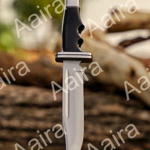 May include: A stainless steel hunting knife with a black handle and silver accents. The blade is curved and the handle has finger grooves for grip. The knife is designed for outdoor use.