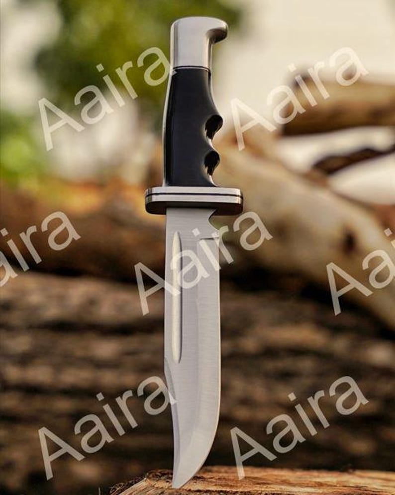 May include: A stainless steel hunting knife with a black handle and silver accents. The blade is curved and the handle has finger grooves for grip. The knife is designed for outdoor use.