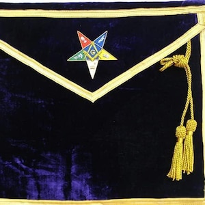 May include: A dark blue velvet apron with gold trim and a colorful star emblem. The apron features a gold rope and tassel detail on the right side. The star emblem has various colors and symbols.