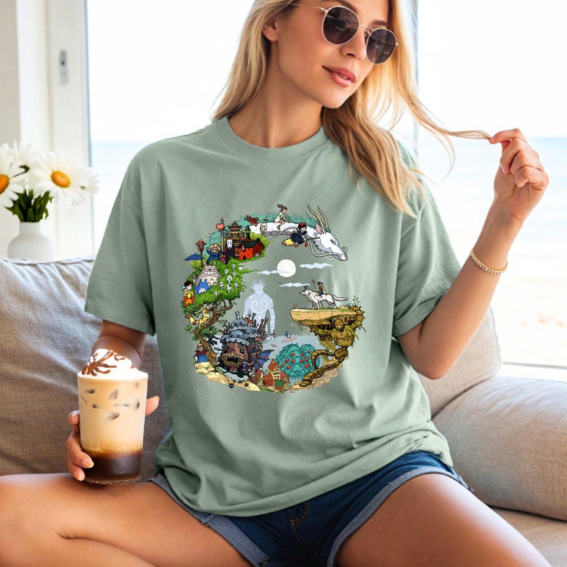 Puede incluir: Camiseta verde salvia con un dise&ntilde;o gr&aacute;fico colorido. El dise&ntilde;o presenta personajes y escenas de una pel&iacute;cula de animaci&oacute;n. La camiseta es de corte holgado y tiene mangas cortas.