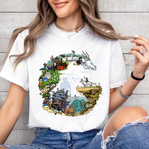 Puede incluir: Camiseta blanca con una ilustraci&oacute;n colorida de un paisaje de fantas&iacute;a, que incluye un drag&oacute;n, un castillo y varios personajes. El dise&ntilde;o est&aacute; dispuesto en forma circular. La camiseta es de tela suave.