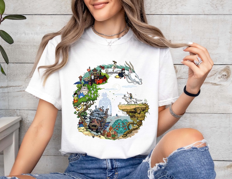 Puede incluir: Camiseta blanca con una ilustraci&oacute;n colorida de un paisaje de fantas&iacute;a, que incluye un drag&oacute;n, un castillo y varios personajes. El dise&ntilde;o est&aacute; dispuesto en forma circular. La camiseta es de tela suave.