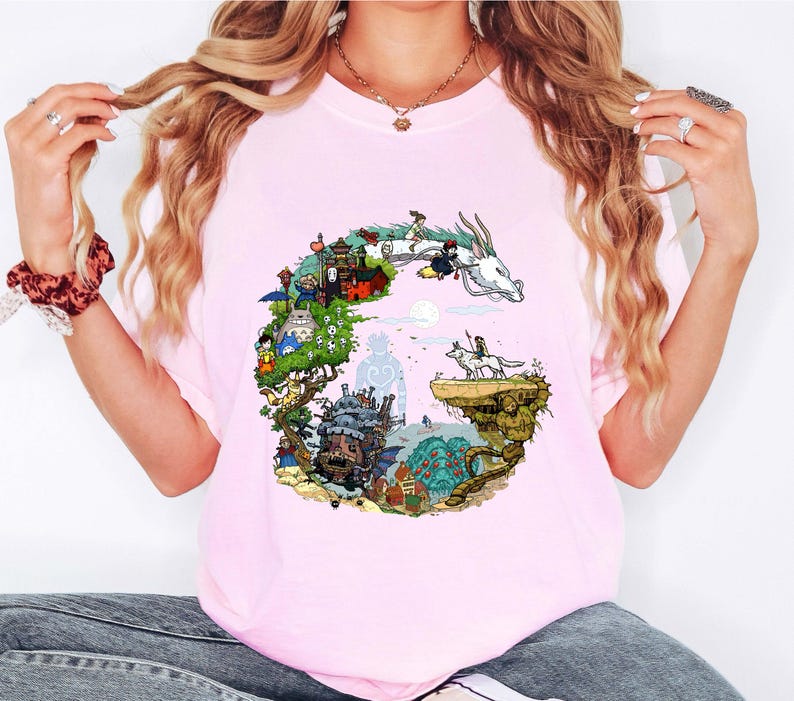 Puede incluir: Camiseta rosa claro con una colorida ilustraci&oacute;n de un drag&oacute;n y personajes de una pel&iacute;cula de animaci&oacute;n fant&aacute;stica. El gr&aacute;fico tiene forma de la letra "G". La camiseta es de material suave.