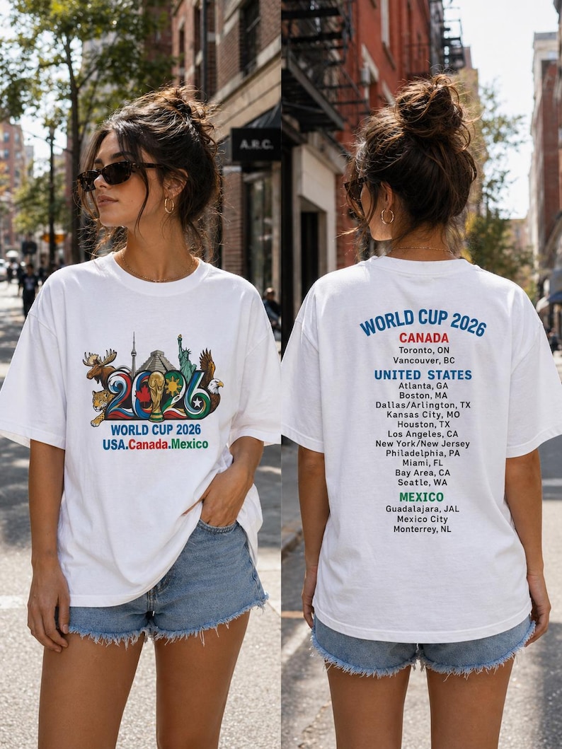 Pode incluir: Uma t-shirt branca com um gr&aacute;fico do World Cup 2026 na frente, incluindo ilustra&ccedil;&otilde;es de um alce, jaguar, &aacute;guia e monumentos. As costas exibem o texto World Cup 2026 com uma lista das cidades-sede no Canad&aacute;, Estados Unidos e M&eacute;xico.