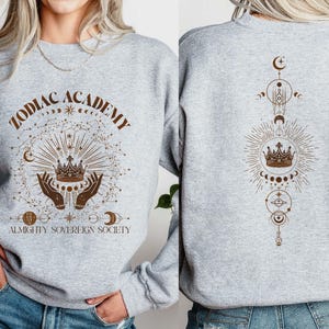 May include: Grey sweatshirt with a brown graphic design featuring a crown, stars, and the text "Zodiac Academy Almighty Sovereign Society".