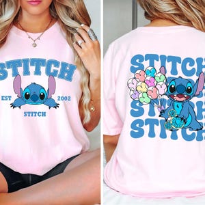 Puede incluir: Camiseta rosa claro con un diseño azul de Stitch y la palabra "STITCH" en texto azul arqueado. El diseño frontal incluye "EST 2002" y "STITCH" debajo. La parte trasera tiene un diseño repetido de Stitch y la palabra "STITCH".