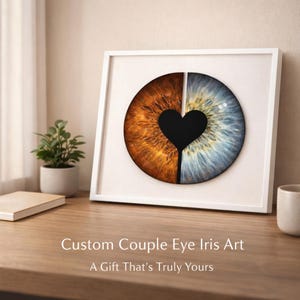 May include: Framed artwork with a split iris design. One half is brown, the other blue, joined by a black heart shape. The text reads "Custom Couple Eye Iris Art" and "A Gift That's Truly Yours."
