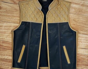 May include: A two-tone leather vest. The upper section is tan and quilted, while the lower section is navy blue. It features a stand-up collar, a zip closure, and two angled pockets. The stitching is light tan.