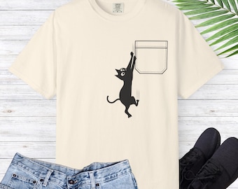 May include: A cream colored t-shirt with a black cat graphic hanging from a pocket. The cat is looking up and has a surprised expression.