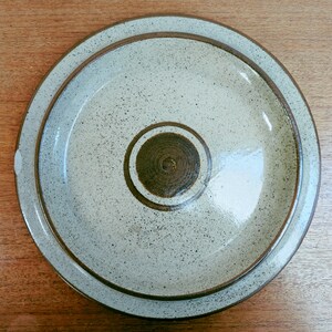 May include: Overhead view of a ceramic plate and lid set. The plate and lid are light beige with dark brown trim and a speckled pattern. The lid has a central, circular design in a darker brown color.