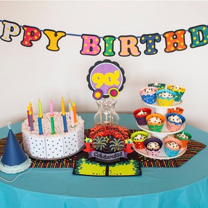 May include: A birthday party table setting with a blue tablecloth, a cake with candles, cupcakes on a tiered stand, and a banner that says "Happy Birthday".