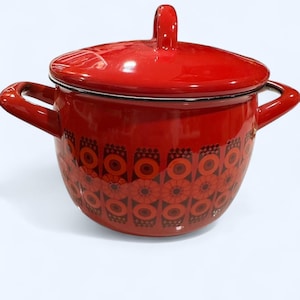 May include: A red enamel pot with a matching lid. The pot features a floral pattern in shades of orange and brown. It has two side handles and a handle on the lid. The pot is designed for cooking and is suitable for kitchen use.
