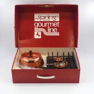 Könnte beinhalten: Ein Vintage-Kocher-Set in Kupferfarbe, in einer roten Box. Auf der Box steht "Spring Switzerland gourmet line". Das Set enthält einen Kupfertopf mit schwarzem Griff, einen Brenner und Utensilien.