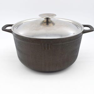 以下が含まれることがあります： 銀色の蓋が付いた黒い鋳鉄製の鍋。鍋には2つの取っ手があり、丸い形をしています。