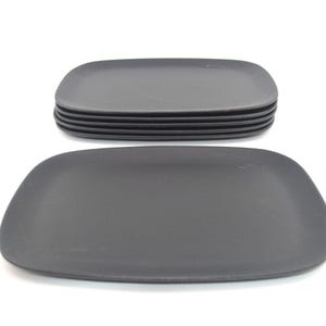 May include: A set of six dark grey, rectangular plates with rounded corners, and one plate in front. The plates are arranged on a white background. The plates have a matte finish.