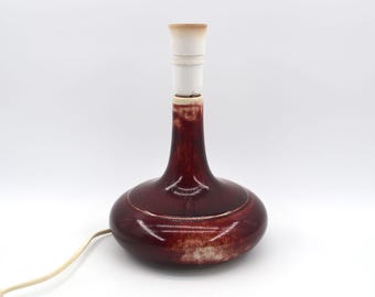 May include: A maroon ceramic table lamp with a bulb socket. The lamp has a rounded base and a slender neck. The lamp is approximately 25 cm tall.