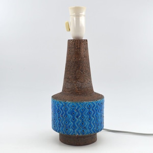 May include: A vintage table lamp with a brown, textured body and a cylindrical blue band with a geometric pattern. The lamp has a white socket and a power cord. A decorative lighting fixture.