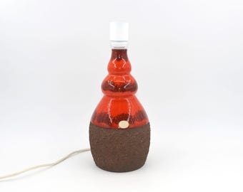 May include: A vintage ceramic table lamp with a bulb socket. The lamp has a red and brown glazed finish and a textured base. This decorative lamp is a unique piece for home decor.